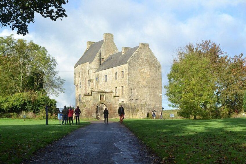 Un bâtiment historique en pierre, auquel mène un chemin pavé, entouré d’arbres et d’herbe. 3