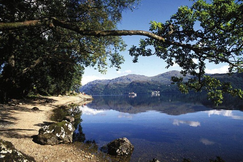 Un lac paisible aux eaux claires, dont le reflet est limpide, entouré d’arbres et bordé de montagnes en arrière-plan. 1