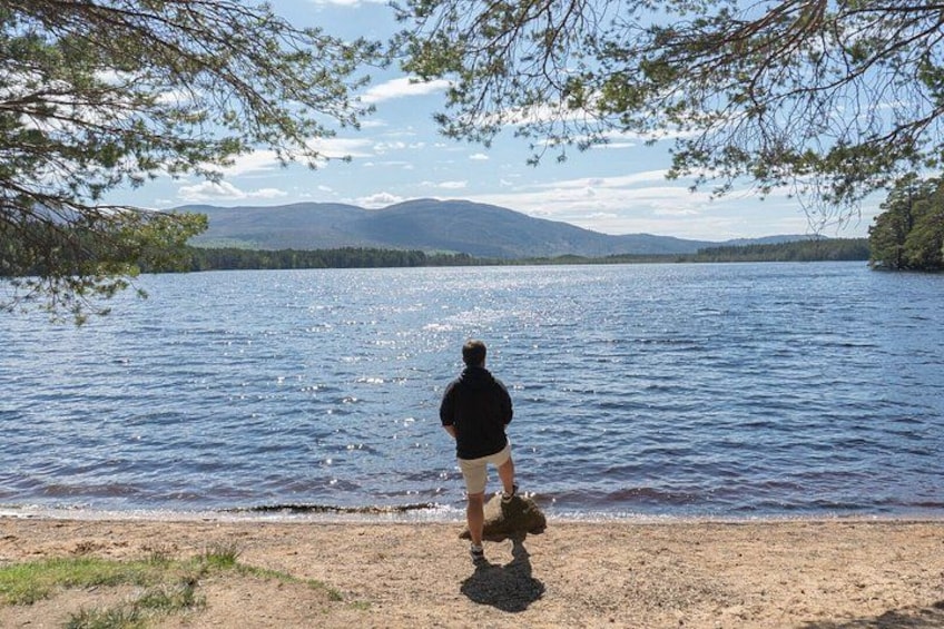 A person standing on a beach facing a lake with mountains in the background. 3