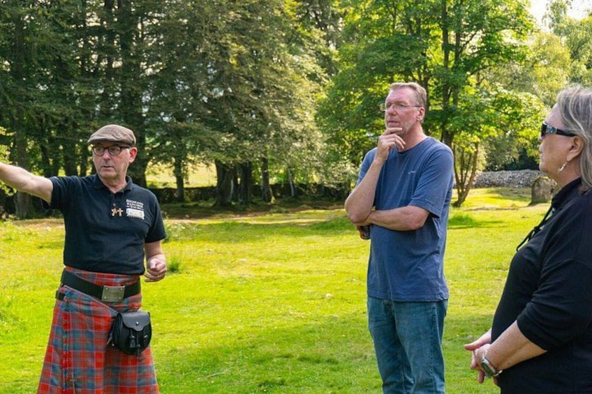 A person in a tartan skirt pointing, two people standing and conversing, and a grassy park with trees. 4