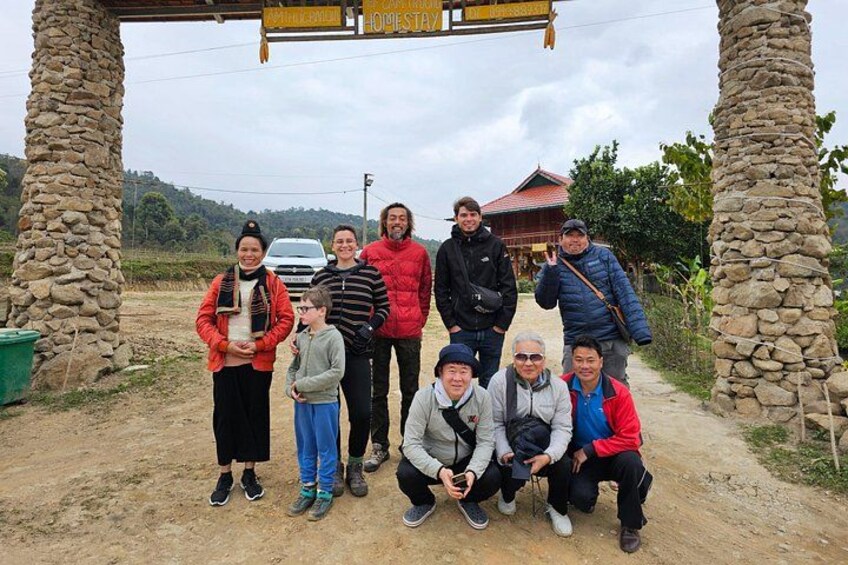 A group of people posing under a stone archway with a dirt path and a building in the background. 2