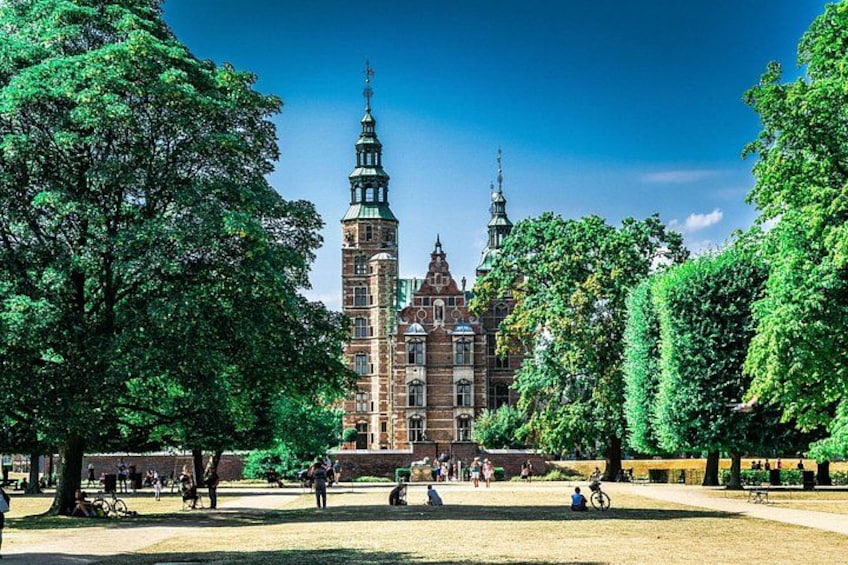 Ein historisches Gebäude mit zwei Türmen, umgeben von Bäumen und Menschen in einem Park. 1