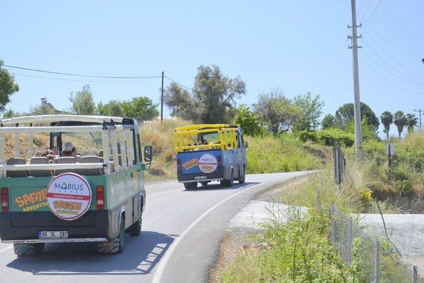 A green safari vehicle and a yellow safari vehicle on a road with vegetation on the sides. 5
