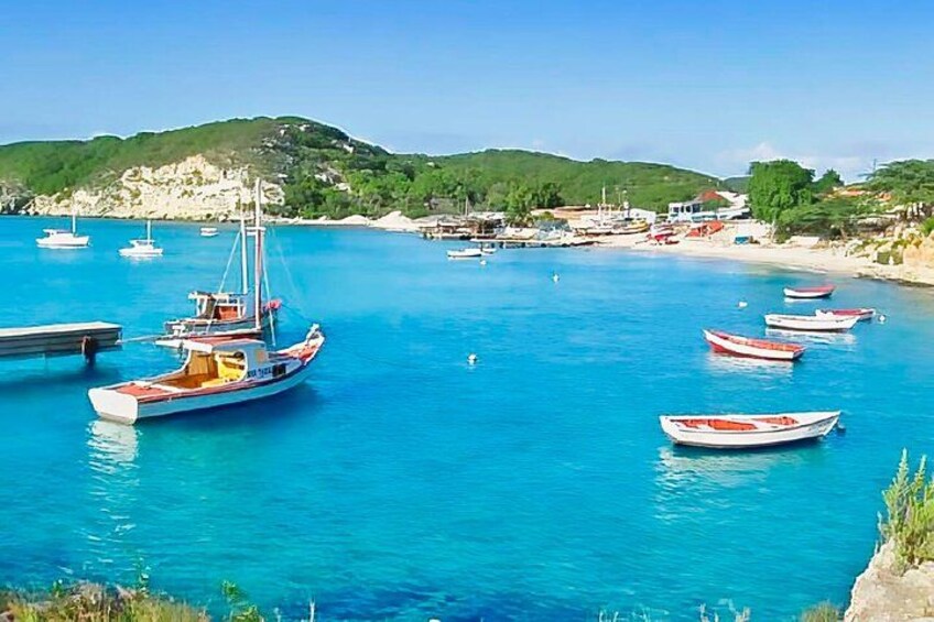 Un paysage côtier avec des bateaux ancrés dans des eaux d’un bleu limpide, une plage de sable et des collines en arrière-plan. 3