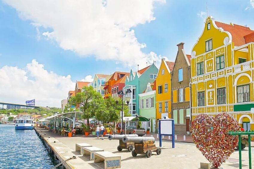 Une promenade en bord de mer bordée de bâtiments aux couleurs vives, avec un canon et une décoration en forme de cœur. 2