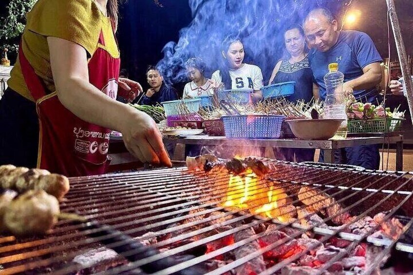 A person grilling meat on a charcoal grill with visible flames. 3