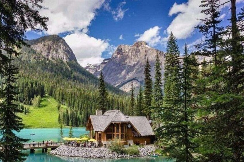 A cabin by a turquoise lake surrounded by mountains and pine trees. 4