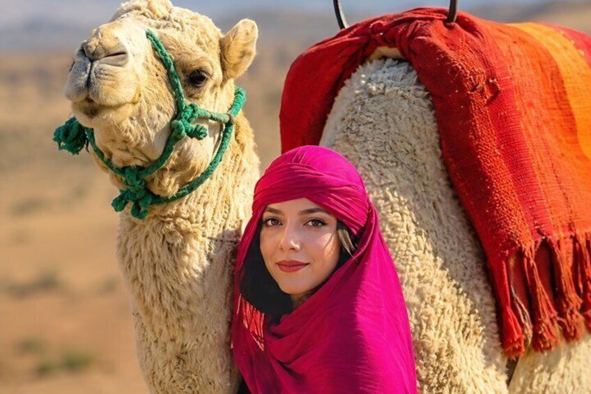 A camel with a rider, both in a desert setting. 5