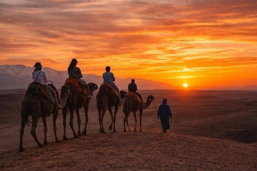 A group of people riding camels on a desert landscape during sunset. 2