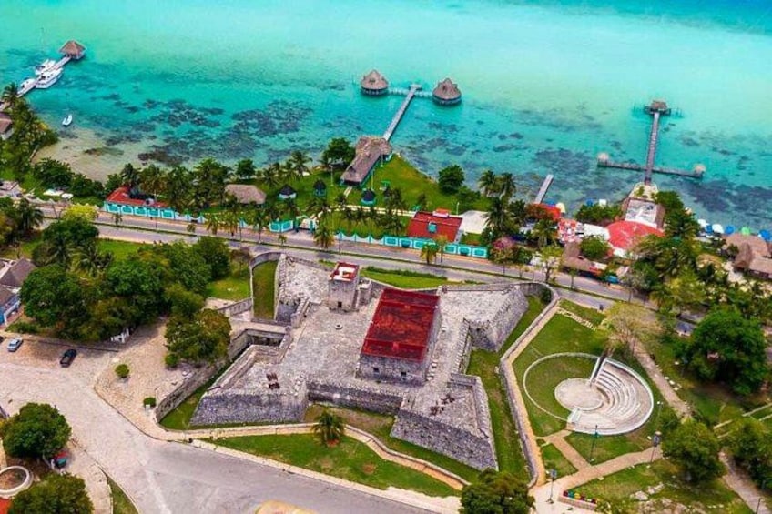 Vue aérienne d’une zone côtière avec une vaste structure ancienne, une jetée et une mer turquoise aux eaux limpides. 2