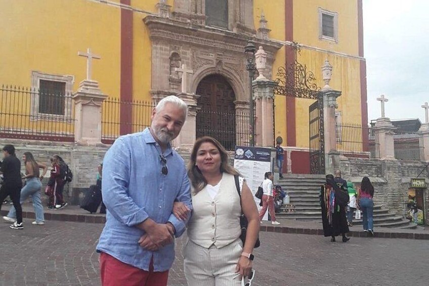 A man and a woman standing in front of a yellow building with a large archway and columns. 5