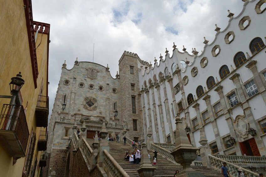 A historic building with ornate architecture, including a bell tower and a staircase leading to the entrance. 2