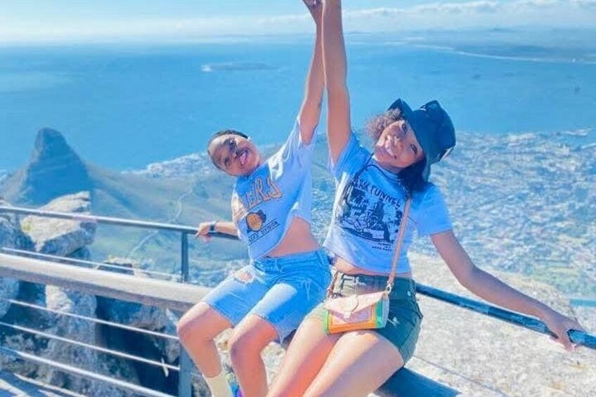 Two people sitting on a railing with a city and ocean in the background. 3