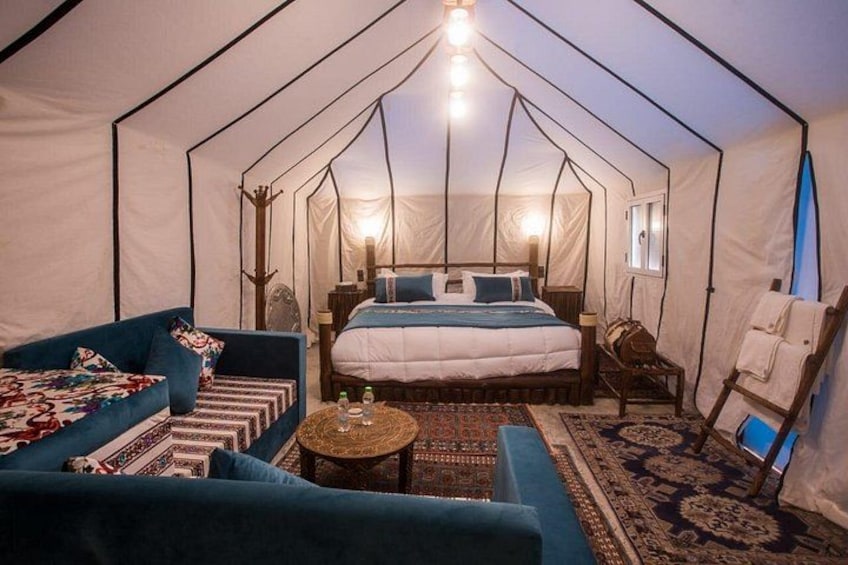 A tented accommodation with a bed, blue sofa, and a small table. 2