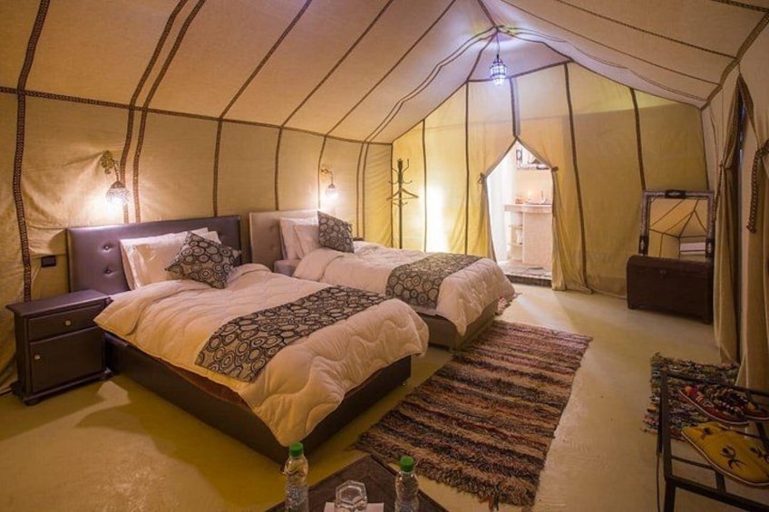 A tented accommodation with two beds, a nightstand, and a small table with a bottle. 4