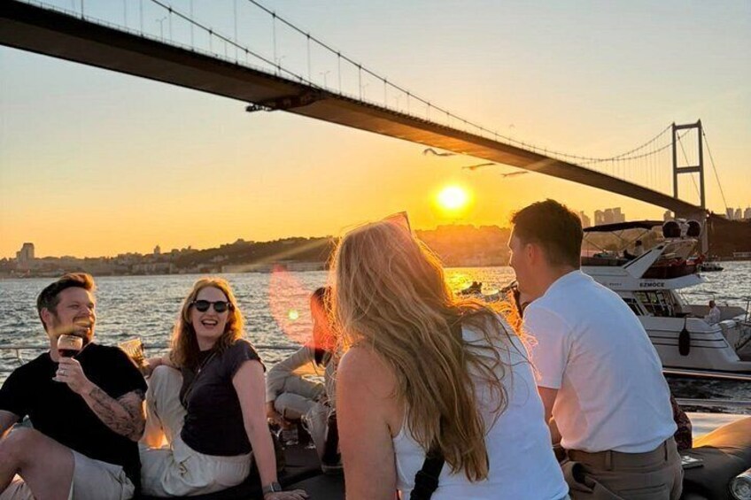 A group of people sitting on a boat near a bridge with the sun setting in the background. 1
