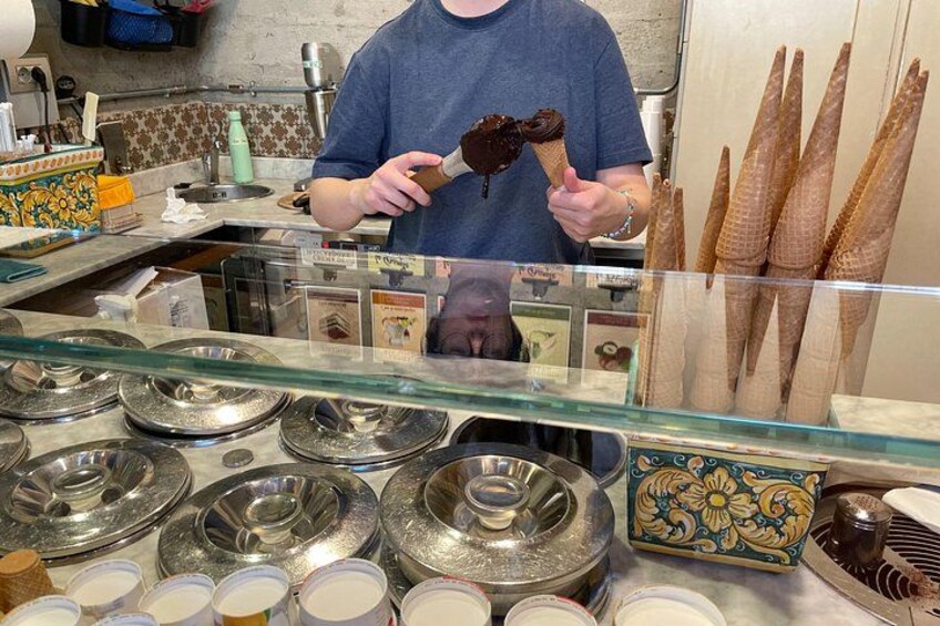 Una persona sosteniendo un cono de helado en una tienda con varios conos y recipientes de helado a la vista. 2