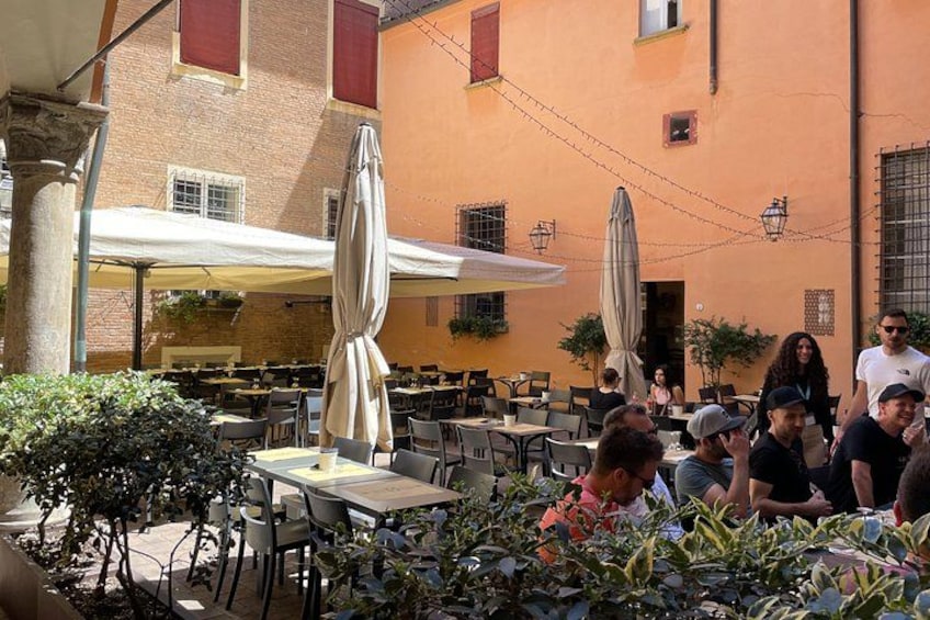 Un café al aire libre con mesas y sombrillas, rodeado de edificios de ladrillo y follaje. 4