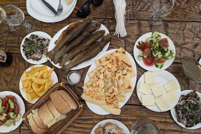 Ein Holztisch mit verschiedenen Speisen, darunter Fisch, Brot, Salat und Fladenbrot. 2