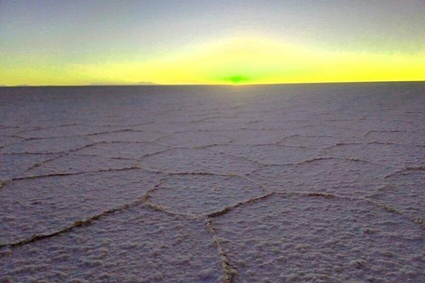 A cracked salt flat with a flat horizon and a sun near the horizon. 4