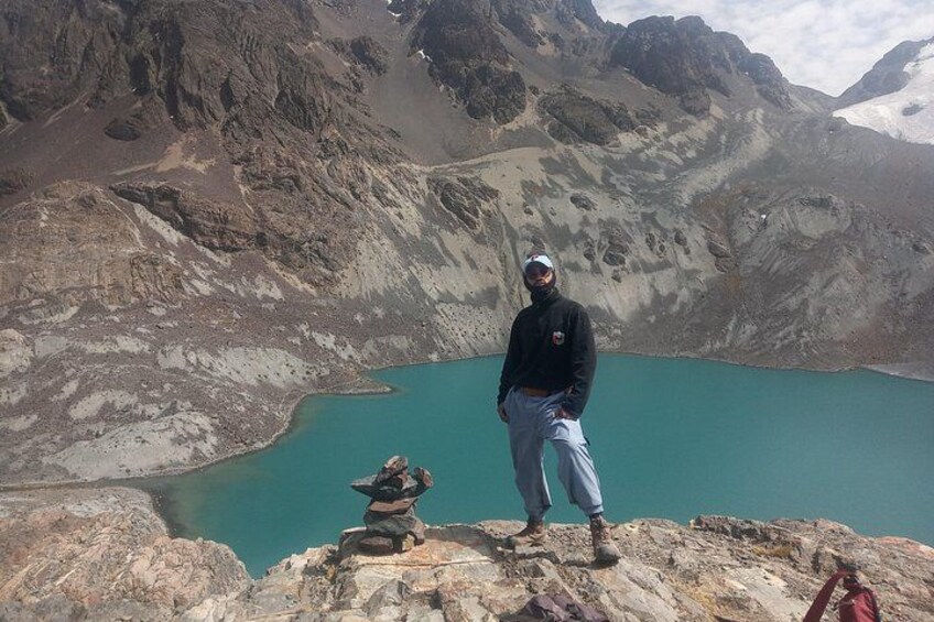 A person standing on a rocky outcrop overlooking a turquoise lake with mountains in the background. 5