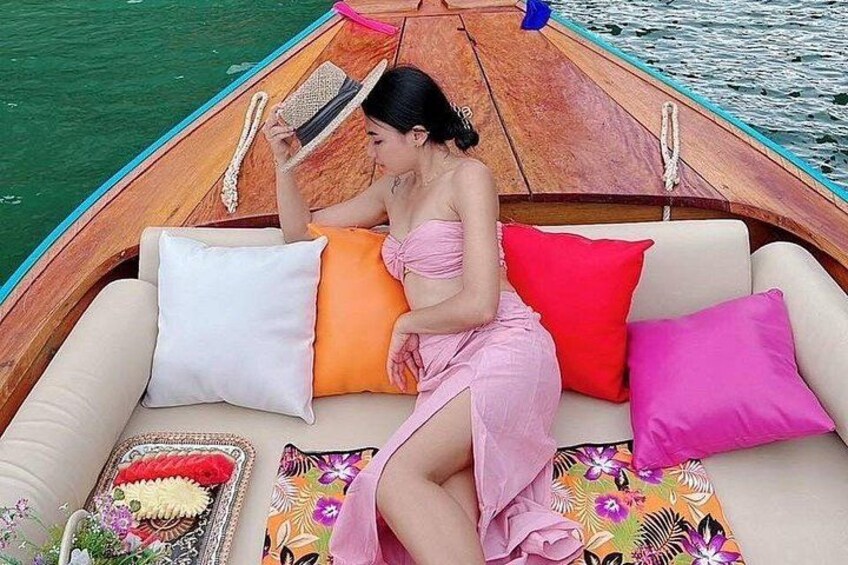 A woman sitting on a boat with colorful cushions and a floral tablecloth. 1