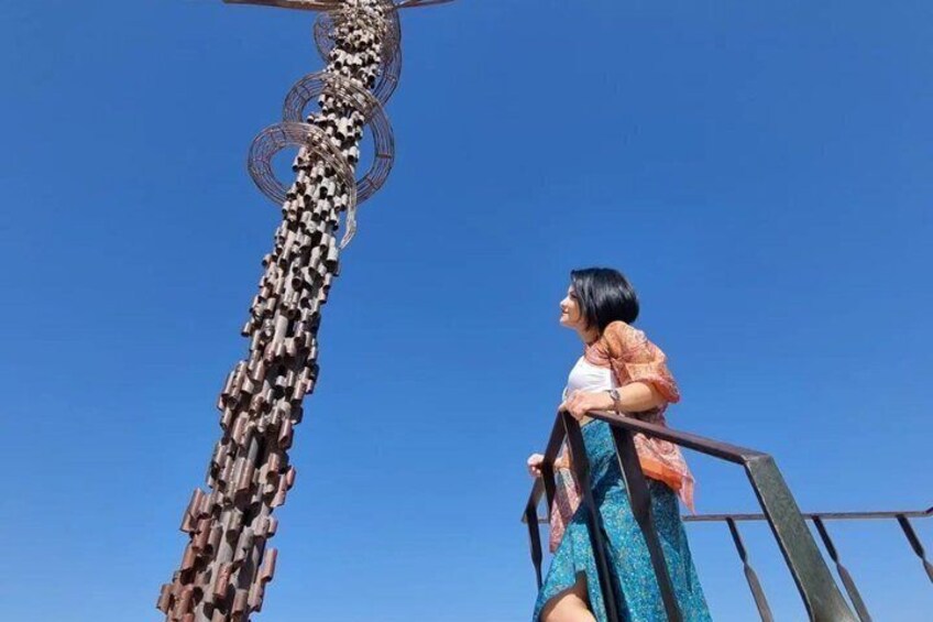 Una persona parada sobre un puente, con una escultura de metal al fondo. 2