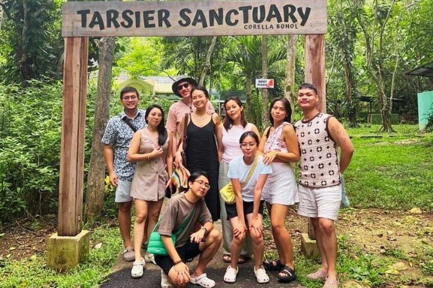 Eine Gruppe von Personen posiert vor einem Schild mit der Aufschrift 'TARSIER SANCTUARY'. 5
