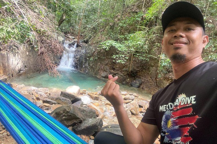 Una persona sentada en una hamaca junto a una cascada en un área boscosa. 1