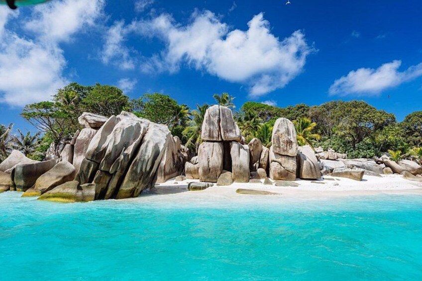 Una playa con grandes rocas, agua turquesa cristalina y palmeras bajo un cielo azul. 1