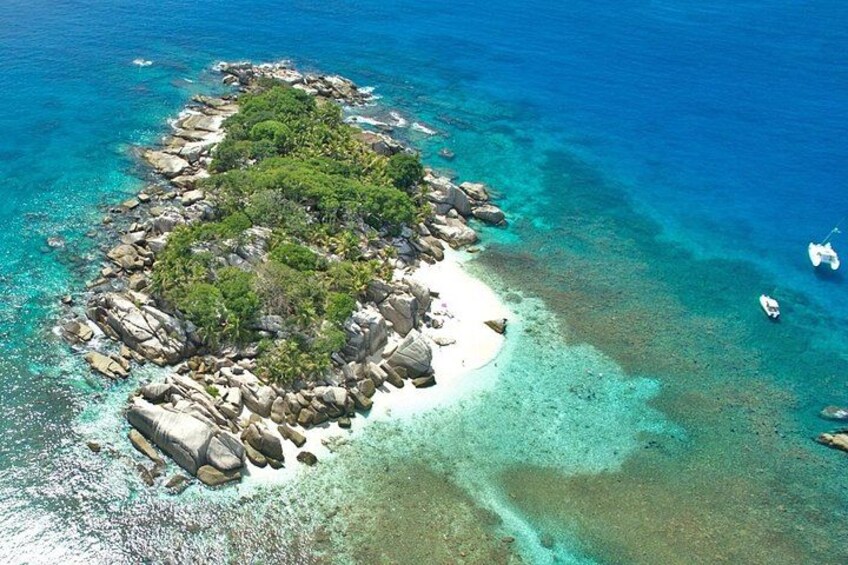 Ein Luftbild einer kleinen Insel mit klarem türkisblauem Wasser, felsigem Gelände und vereinzelter Vegetation. 4