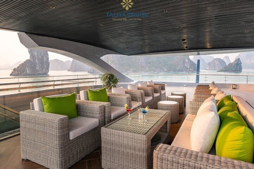 A modern outdoor lounge with wicker furniture and a view of the sea. 3