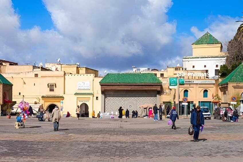 Una plaza animada con edificios históricos, una estructura destacada con techo verde y un cielo azul despejado. 5