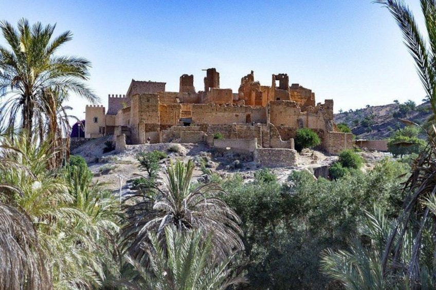 Una antigua fortaleza de piedra con ruinas, rodeada de palmeras y vegetación seca. 3