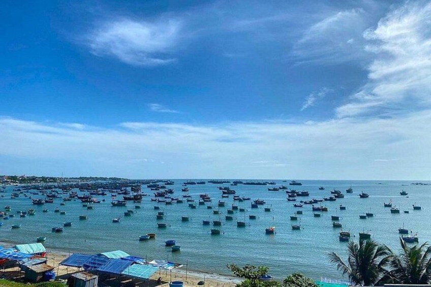 Una zona costera con numerosos barcos fondeados en el agua, cielo despejado y una playa con construcciones. 2