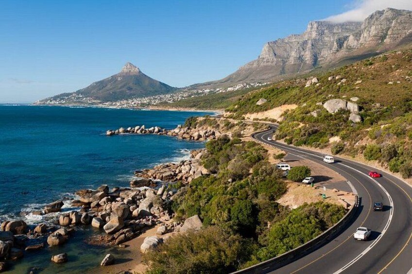 A coastal road with vehicles, a mountain, and the ocean. 5
