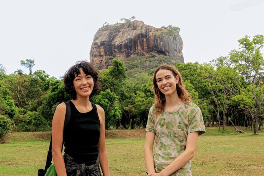 Two people standing in a grassy area with a large rock formation in the background. 1