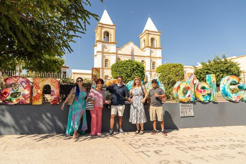 Un grupo de personas frente a letras coloridas que deletrean 'Cecilia', con una iglesia al fondo. 3