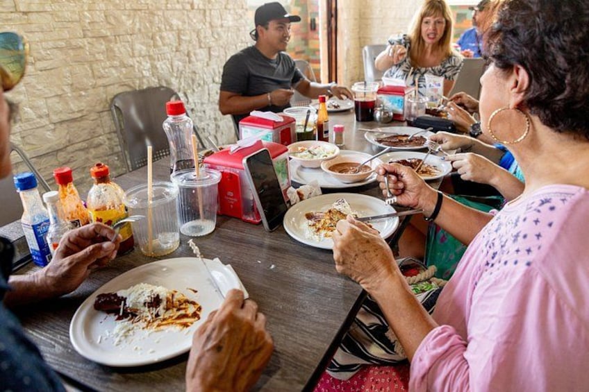 Personas comiendo en una mesa con recipientes de comida y bebidas. 2