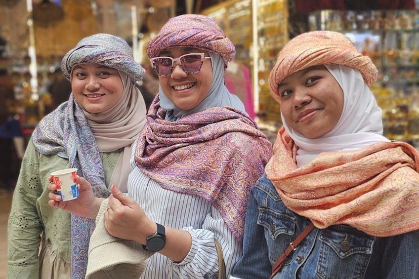 Drie personen op een markt, met spullen op de achtergrond. 3
