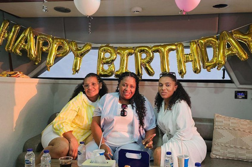 Drie personen zitten aan een tafel, erboven een 'HAPPY BIRTHDAY' ballonbanner. 4