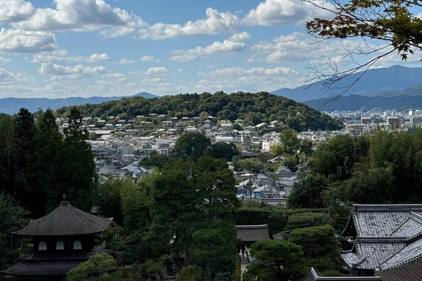 A cityscape with traditional buildings, a hill with greenery, and mountains in the distance. 3