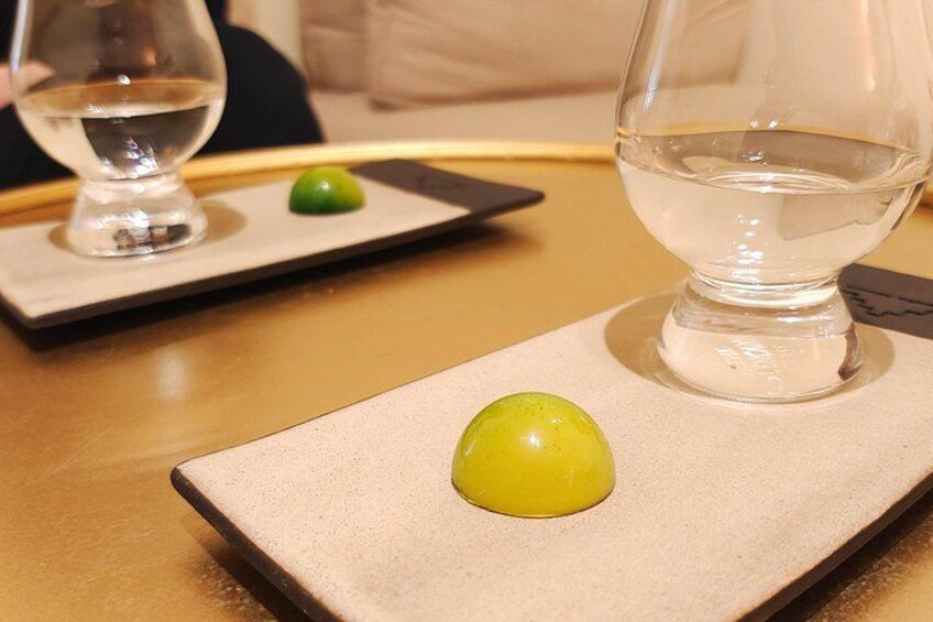 Una mesa con un vaso de agua y dos objetos verdes pequeños sobre un plato rectangular. 5