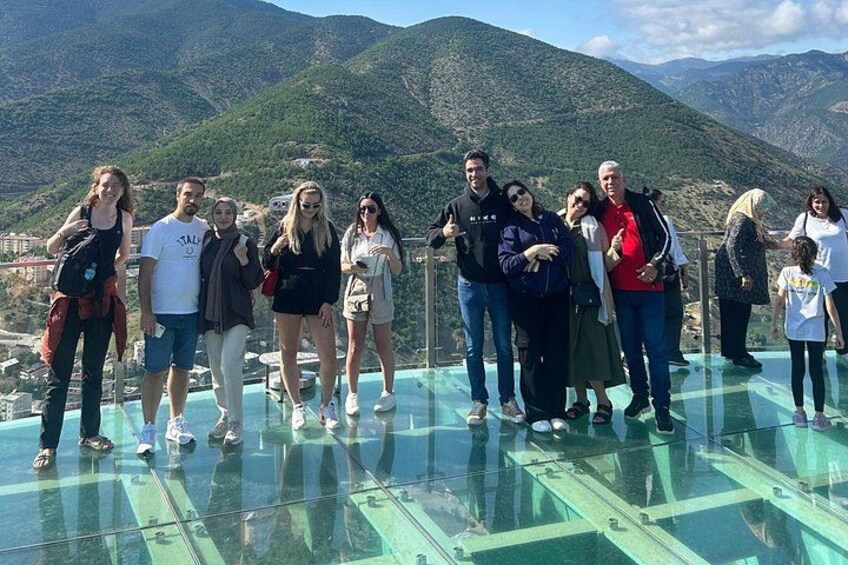 A group of people standing on a glass bridge with a mountainous landscape in the background. 5