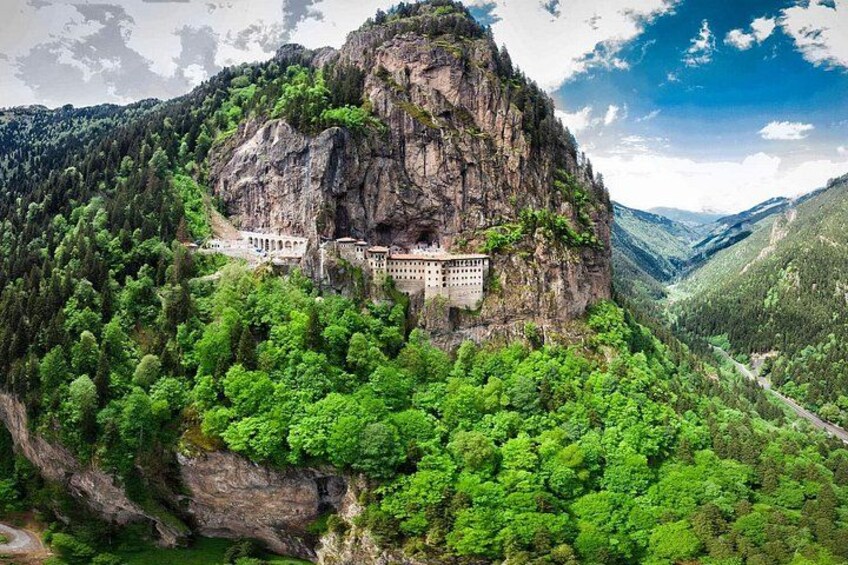 A monastery on a cliff surrounded by lush greenery. 1
