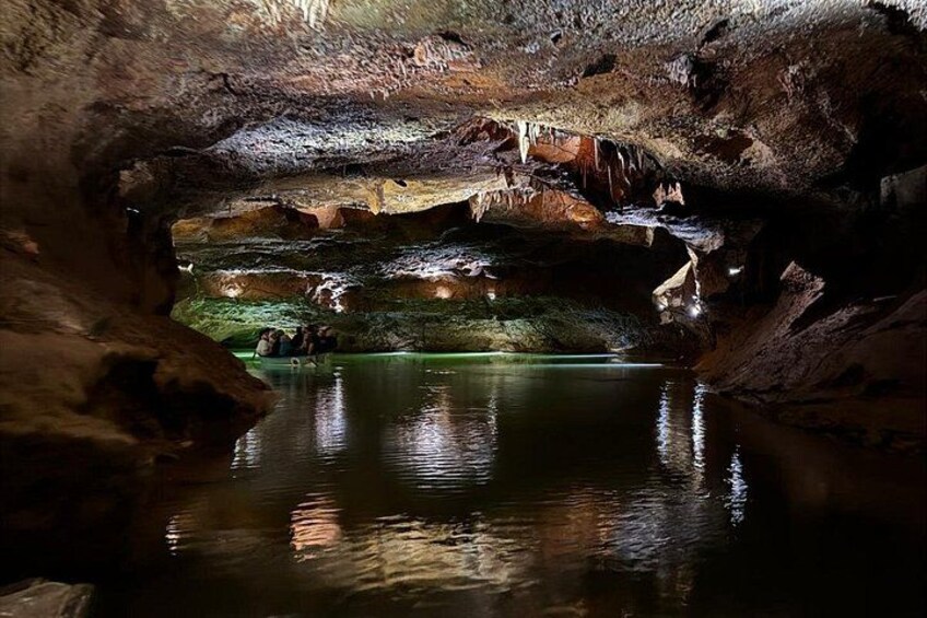 A cave interior with stalactites, a water pool, and a cave opening. 5