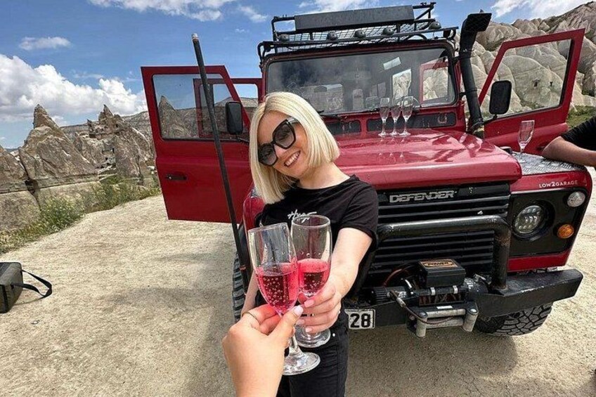 A person holding a wine glass in front of a red Defender vehicle with a license plate number 28. 3