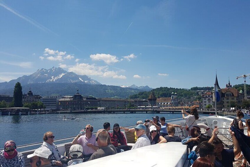 Un recorrido en barco con pasajeros disfrutando de vistas a un lago, montañas y edificios al fondo. 2