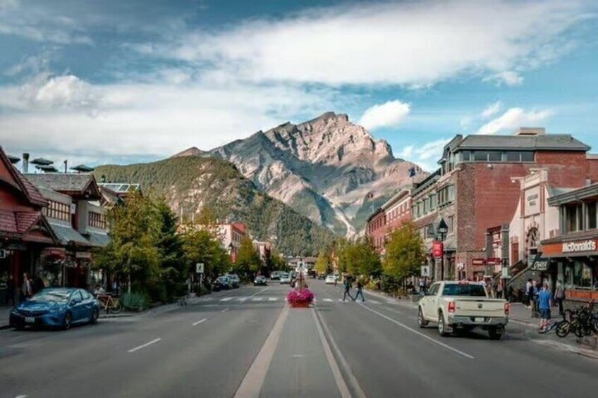 A mountain town street with cars, buildings, and a prominent mountain in the background. 4