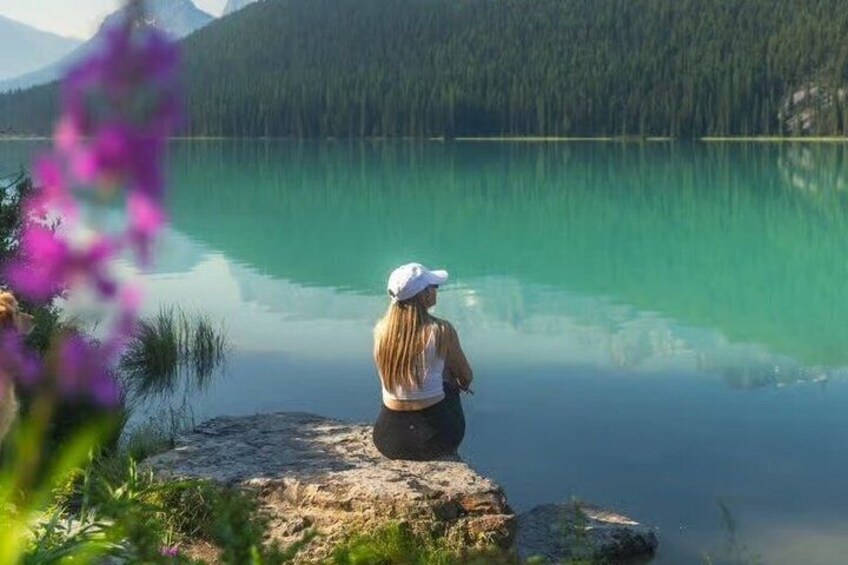 A person sitting on a rock by a calm lake with mountains in the background. 2